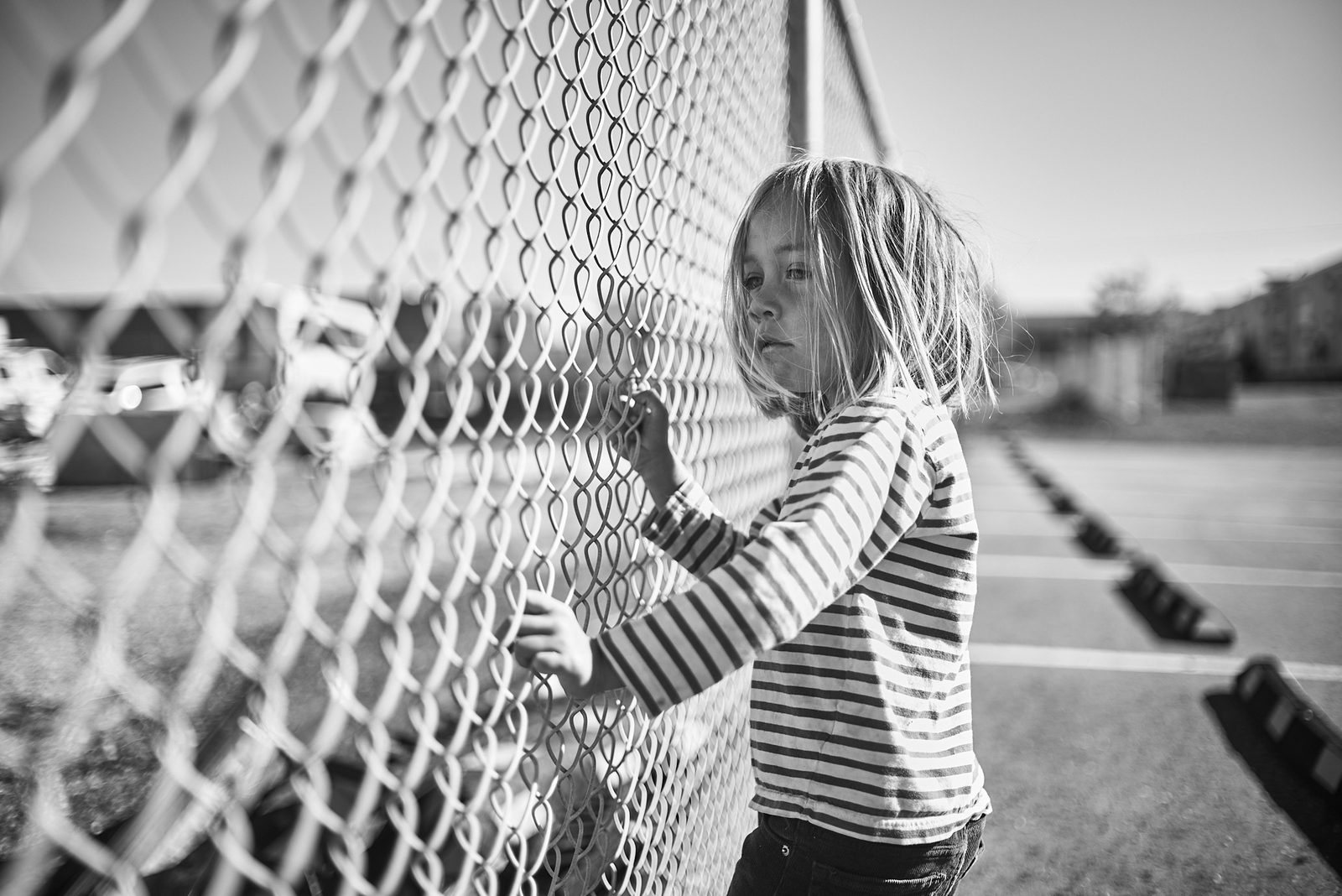 Child at chain link fence in afternoon light — black and white portrait photography