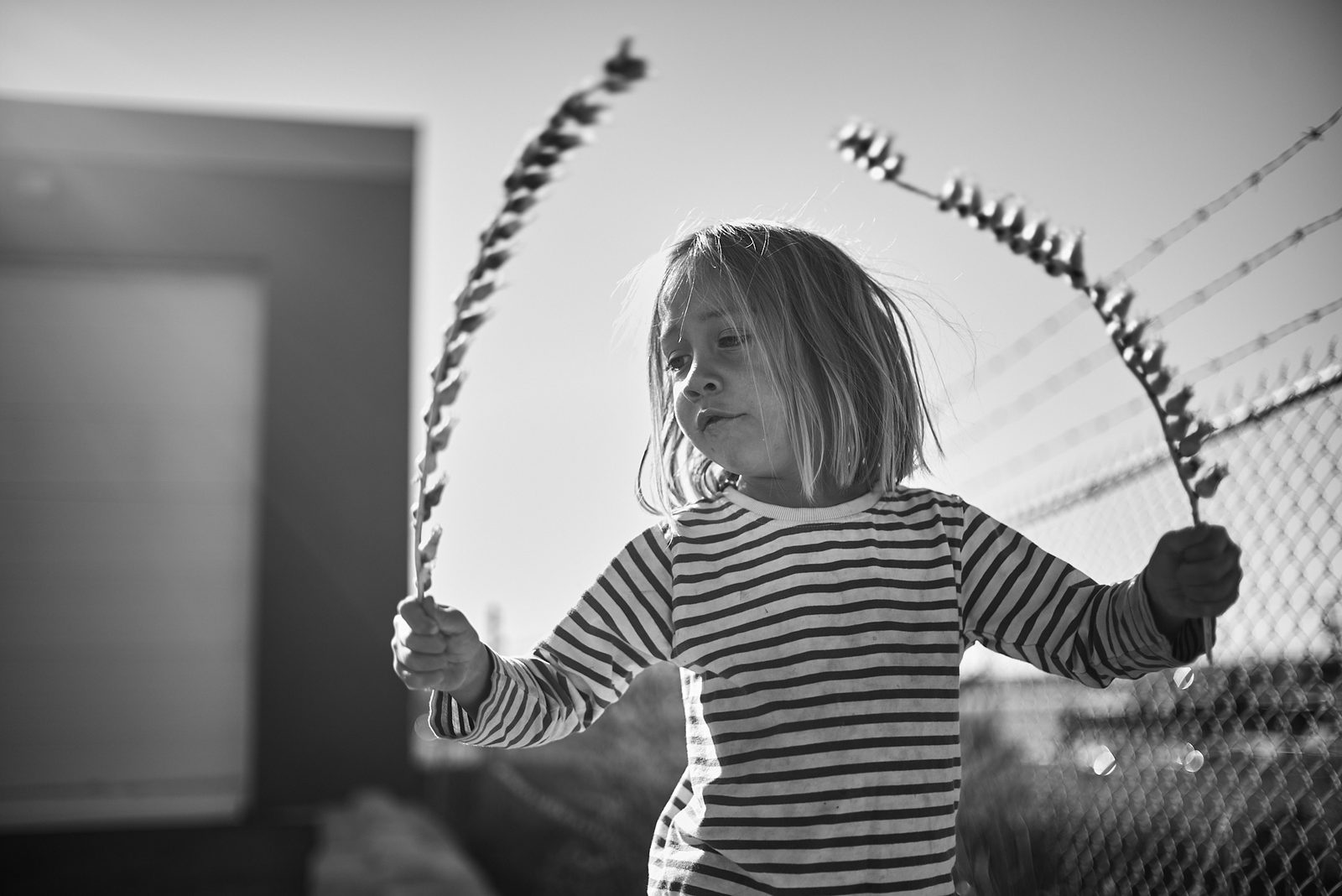 Child with hula hoop backlit by fence — black and white action photography