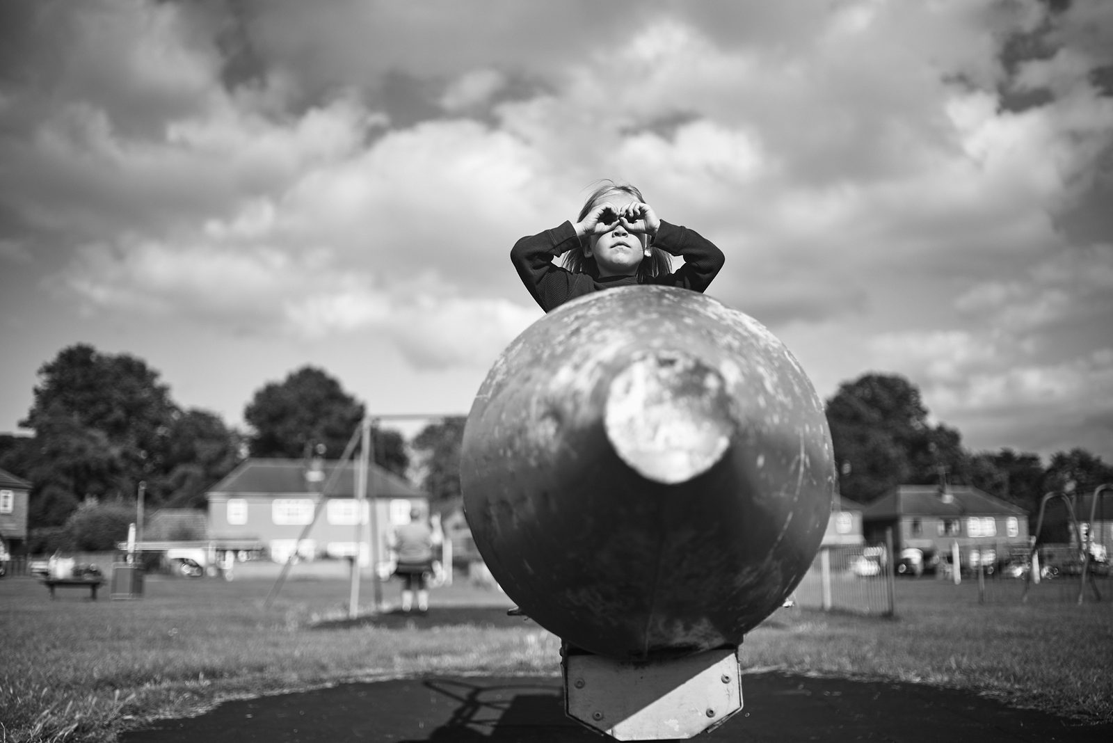 Child on playground rocket under dramatic clouds — black and white photography