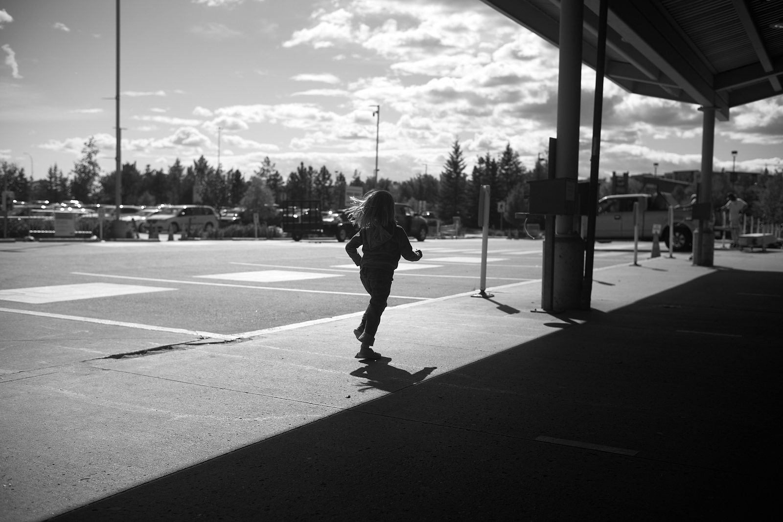 Child running through empty parking lot in harsh shadow — black and white street photography