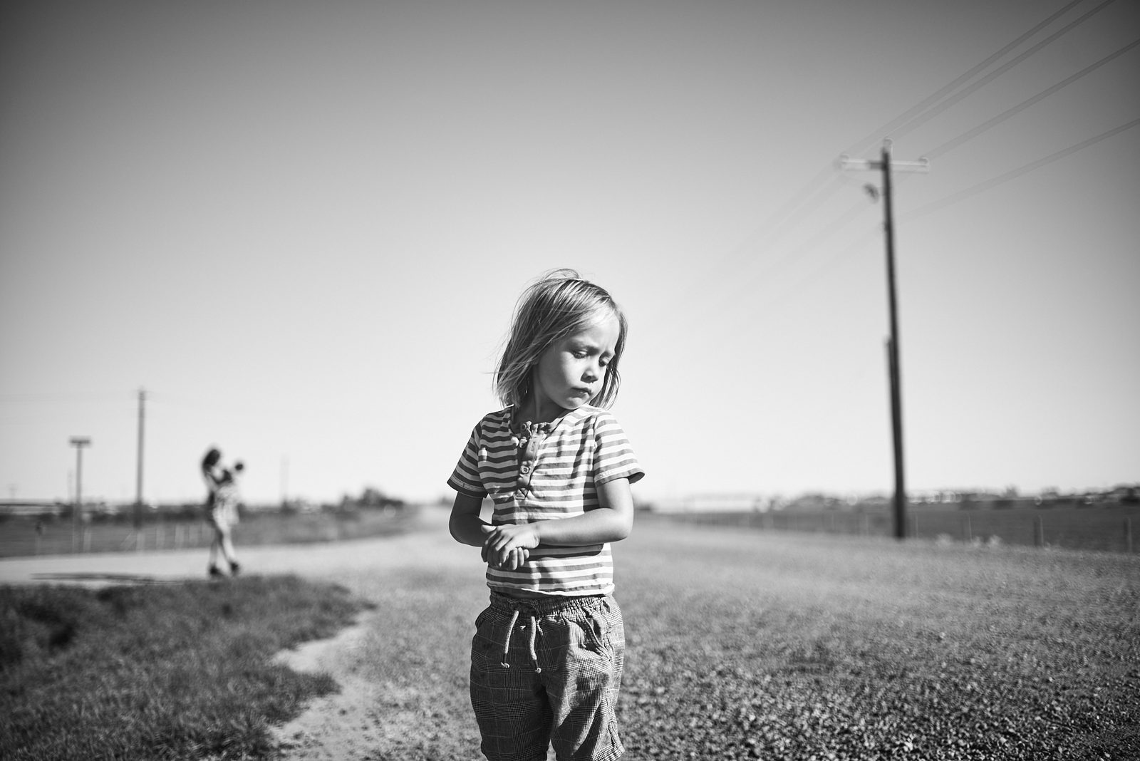 Child walking along prairie road with powerlines — black and white street photography Alberta