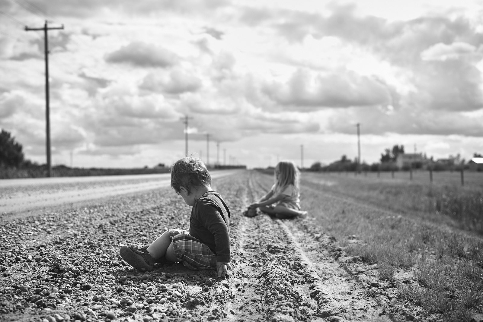 Children sitting on gravel road on the prairies — black and white documentary photography