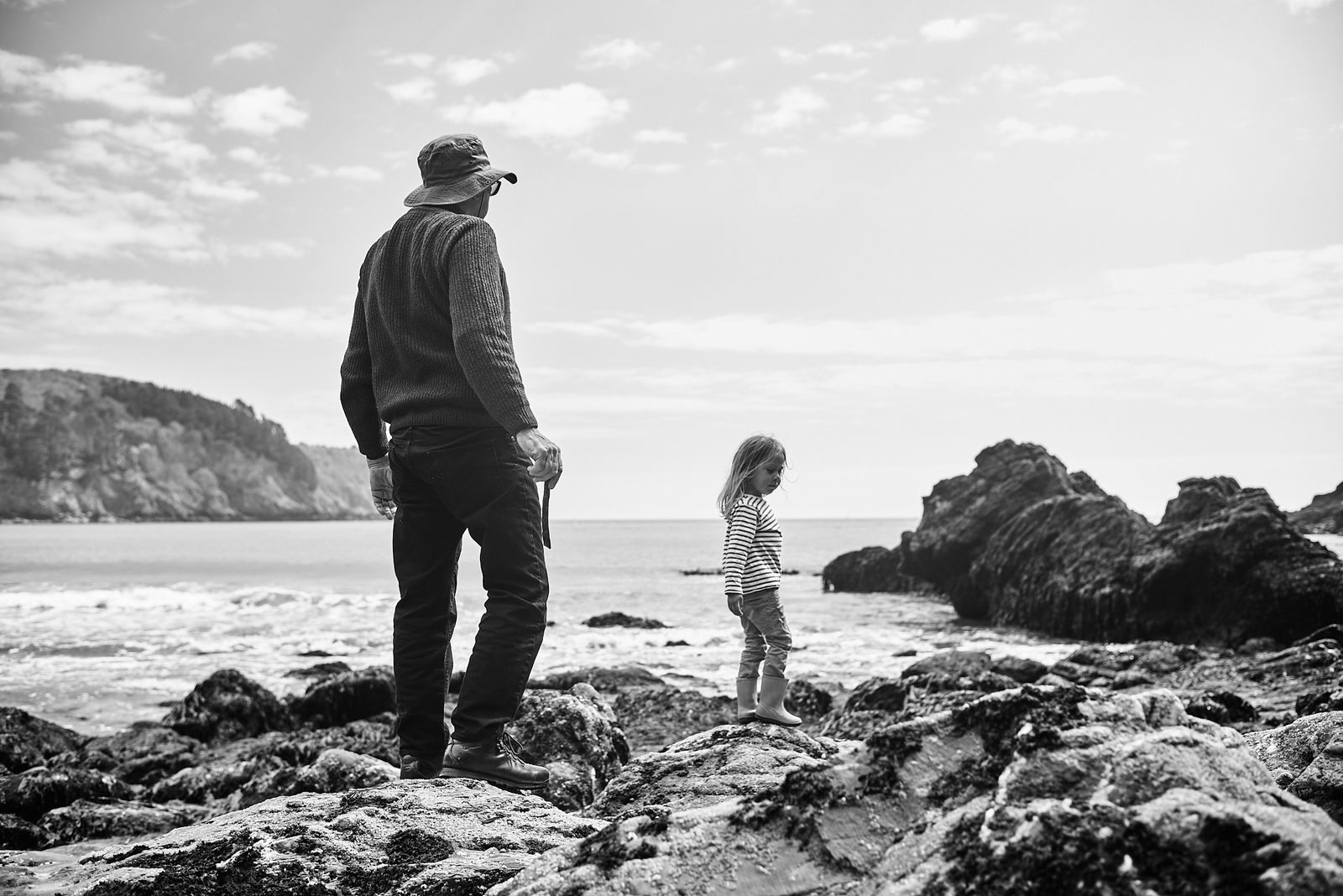 Father and daughter on rocky coast looking at ocean — black and white family photography