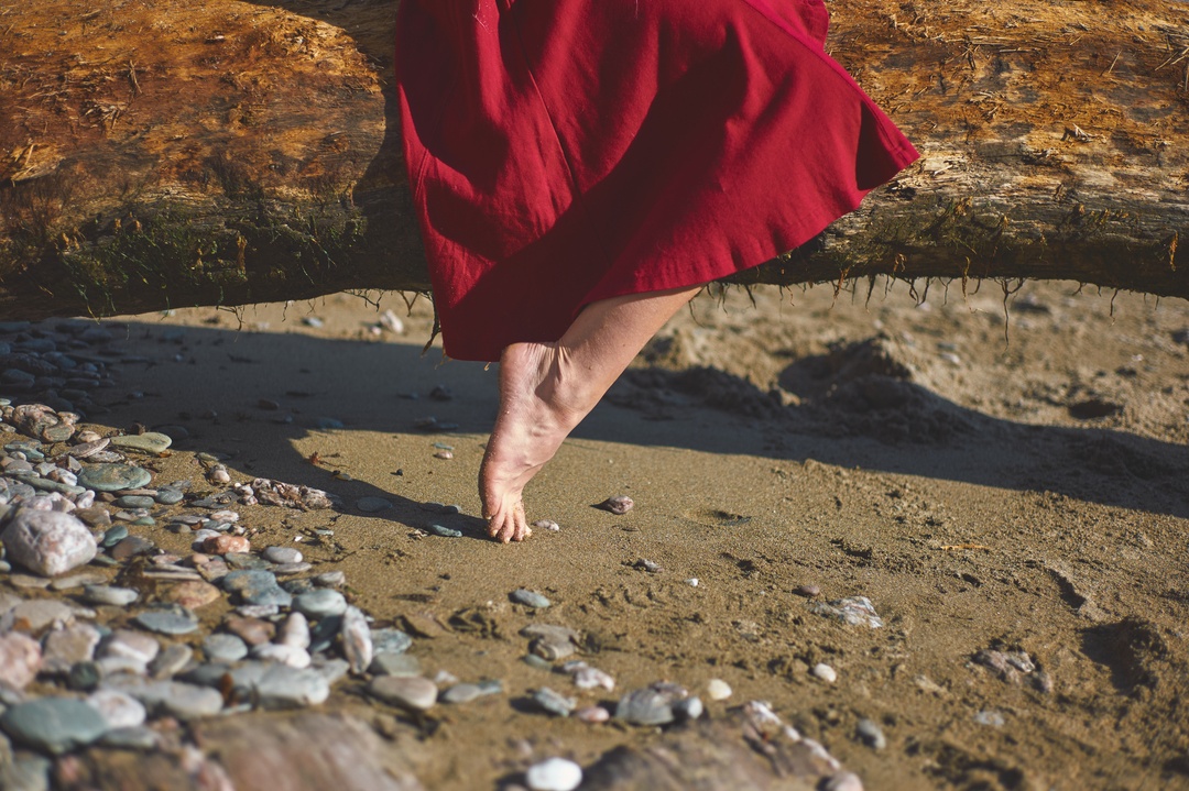 Bare feet in red dress on pebble beach — fashion detail photography