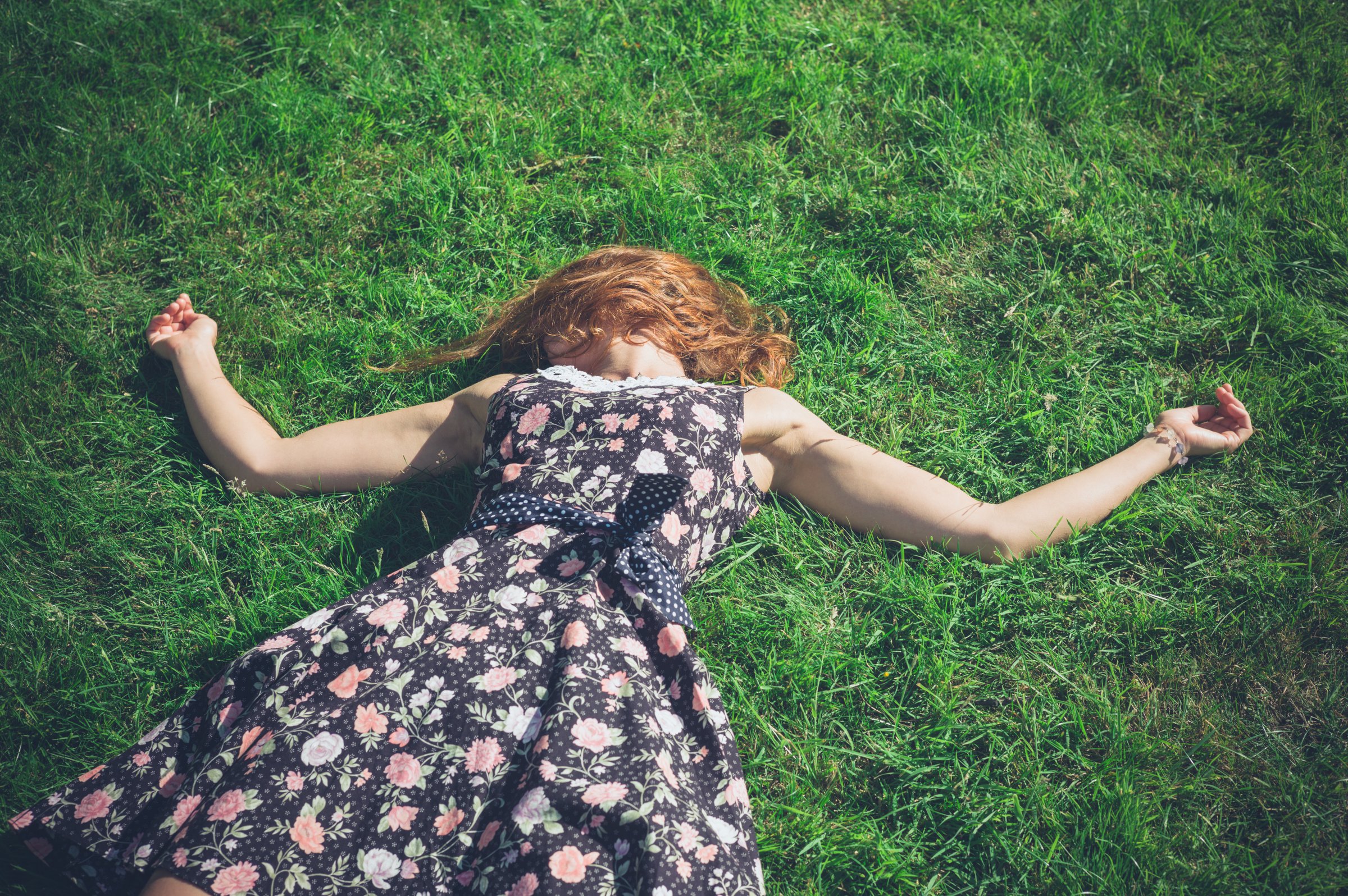 Red-haired woman in floral dress lying on grass — natural light portrait photography