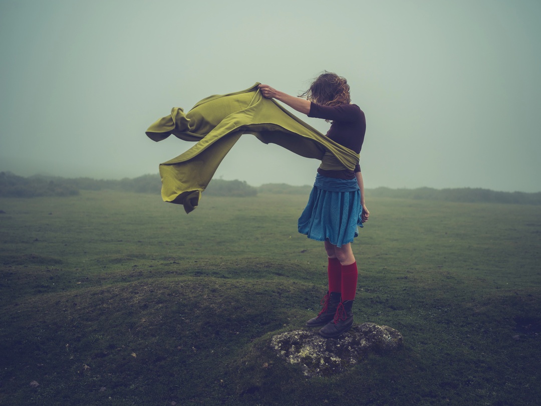 Woman with coat billowing in wind on misty moorland — editorial photography