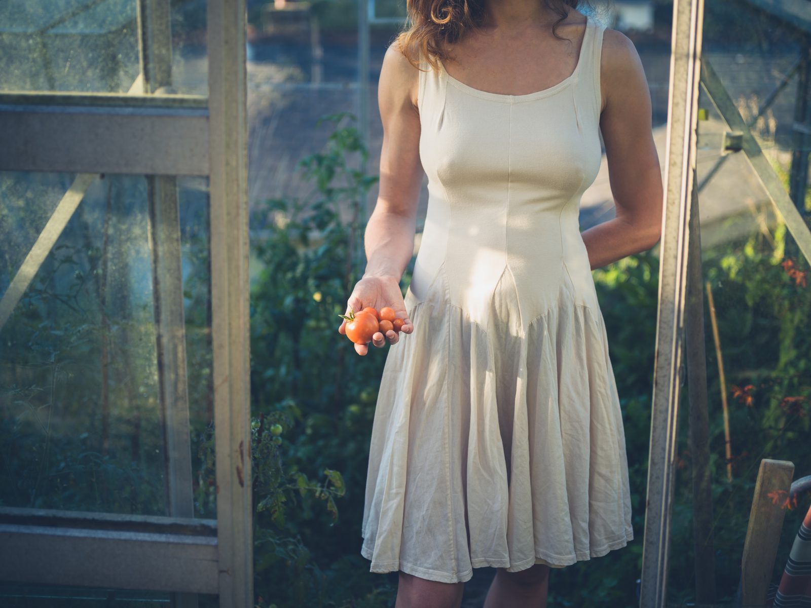 Woman in white dress in greenhouse at sunset — natural light editorial photography